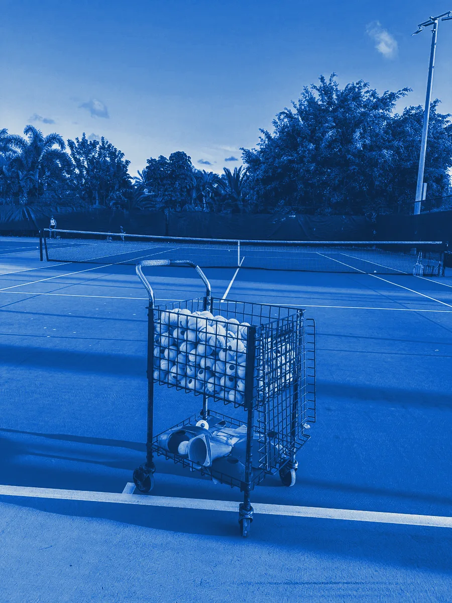 A cart of tennis balls on an empty hard court