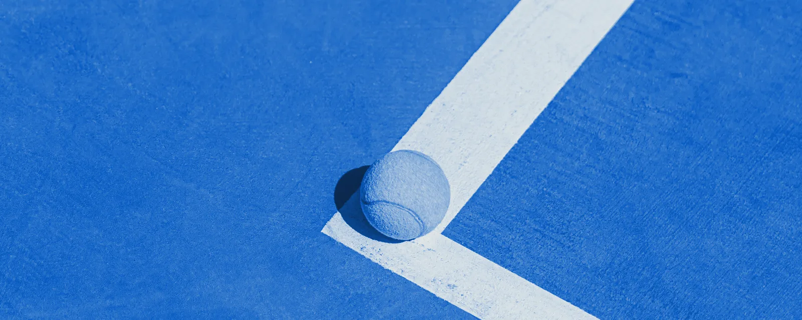 A tennis ball resting on the painted corner line of a court
